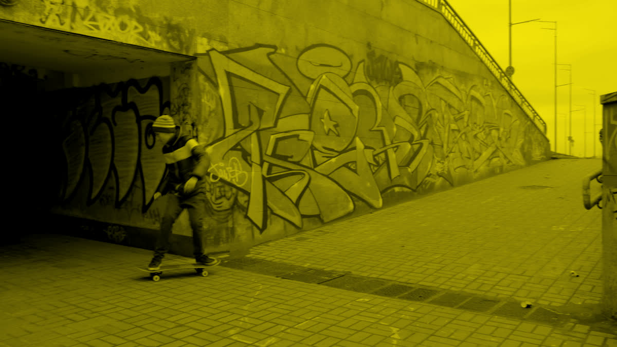 Skateboarder passing a graffiti wall, yellow duotone